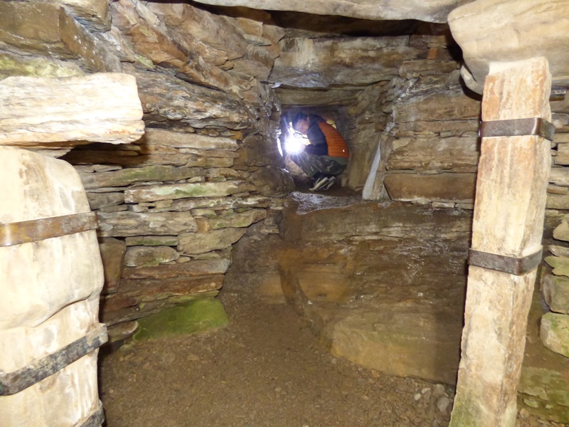 Person crawling along the tight narrow entrance tunnel at Rennibister Earth House